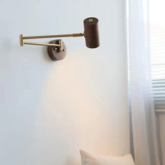 Close-up of a wall sconce with a dark wood cylinder lamp head and a brass swing arm, highlighting the texture of the wood and the finish of the metal.