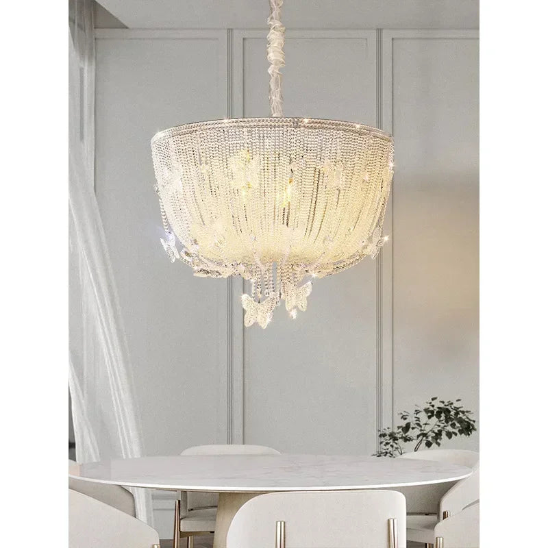 A polished chrome crystal waterfall pendant light with clear crystal accents hanging above a white marble table in a well-lit room.