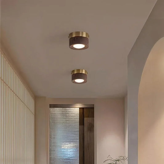 A pair of flush mount ceiling lights with black walnut wood and brass finishes illuminating a hallway.