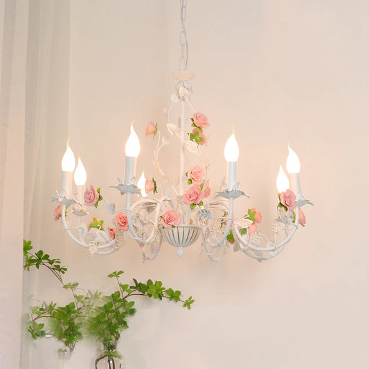 A white iron chandelier adorned with pink roses and green leaves, suspended from a chain.