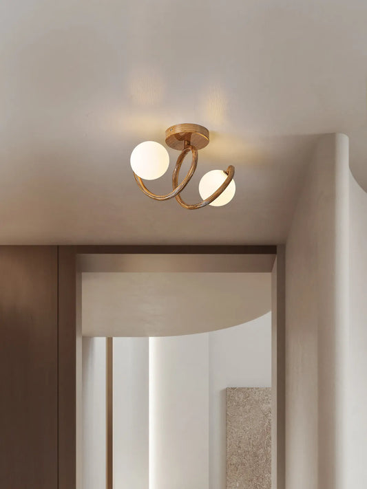 A brushed gold semi-flush ceiling light with intertwined swirl arms and frosted globes, mounted on a white ceiling in a hallway.