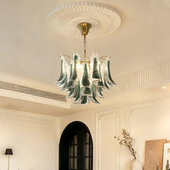 A gold-tone floral-inspired chandelier with green and clear glass drops, installed in a room with white moldings and arched doorways.