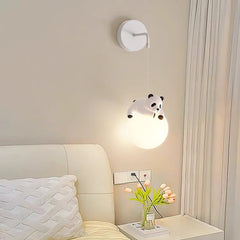 White resin panda figurine hanging from a cord pendant light with a glowing white globe, mounted on a wall with a plug socket below.
