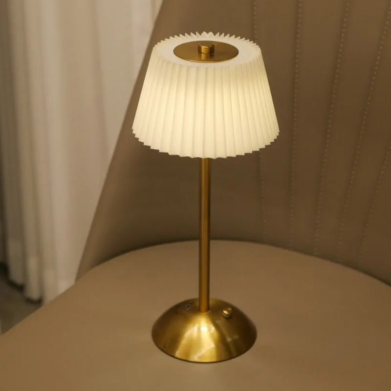 Table lamp with pleated white shade and gold base on a beige surface.