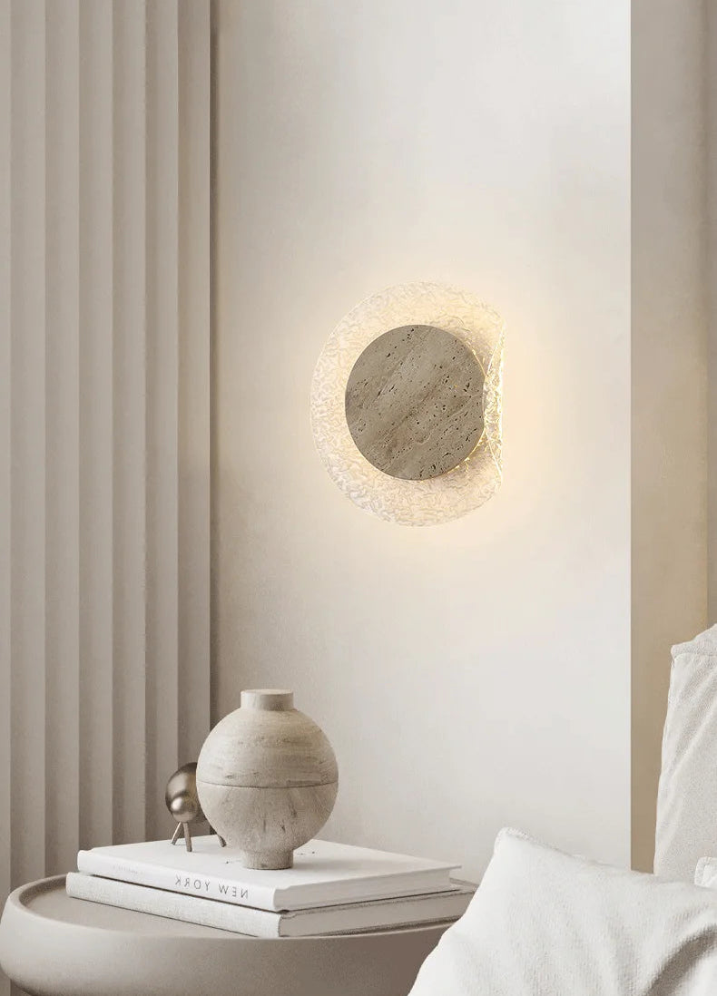 Round wall light fixture on a neutral wall with books and a vase on a table.