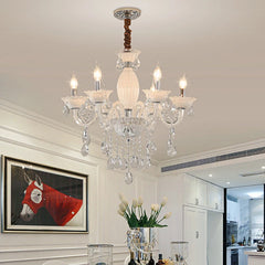 A black and crystal candelabra chandelier with five illuminated bulbs, installed in a dining room setting with artwork and flowers.