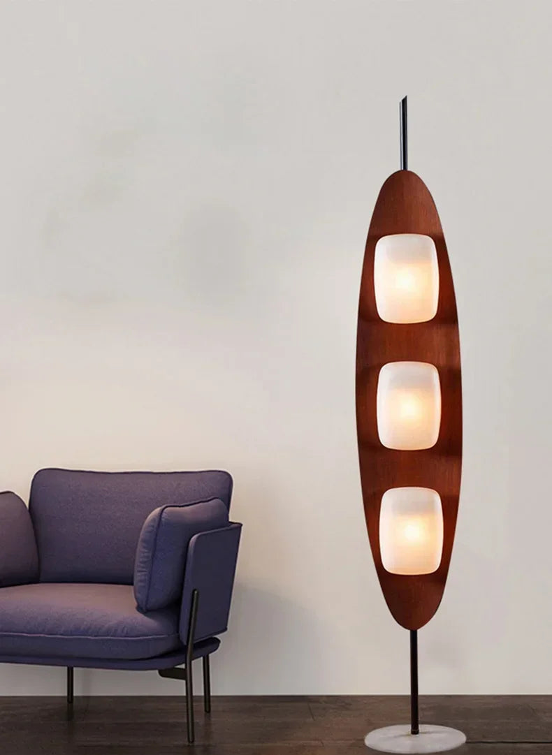 Modern floor lamp with three light fixtures next to a purple armchair on a plain background