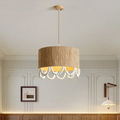 A rattan drum pendant light with a draped wooden bead accent hanging in a room with decorative wall molding and artwork.