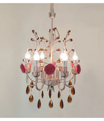 Close-up view of a pink and gold chandelier with ceramic rose accents and hanging amber crystals.