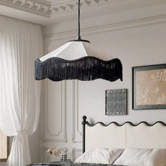 Fabric fringe pendant light with a white shade and black fringe, hanging in a bedroom setting above a bed.