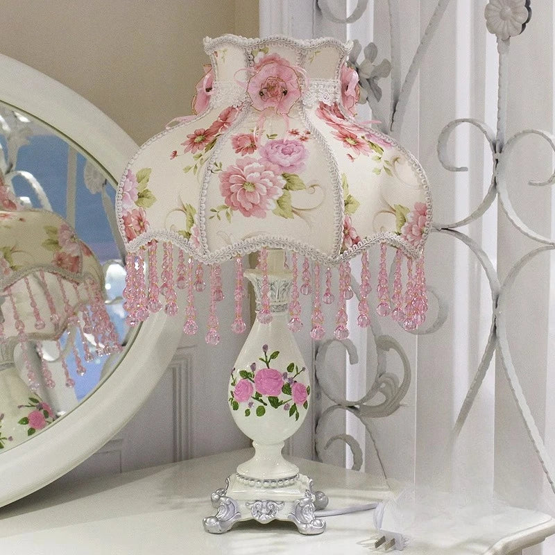 Decorative lamp with floral design and pink beads on a white surface.