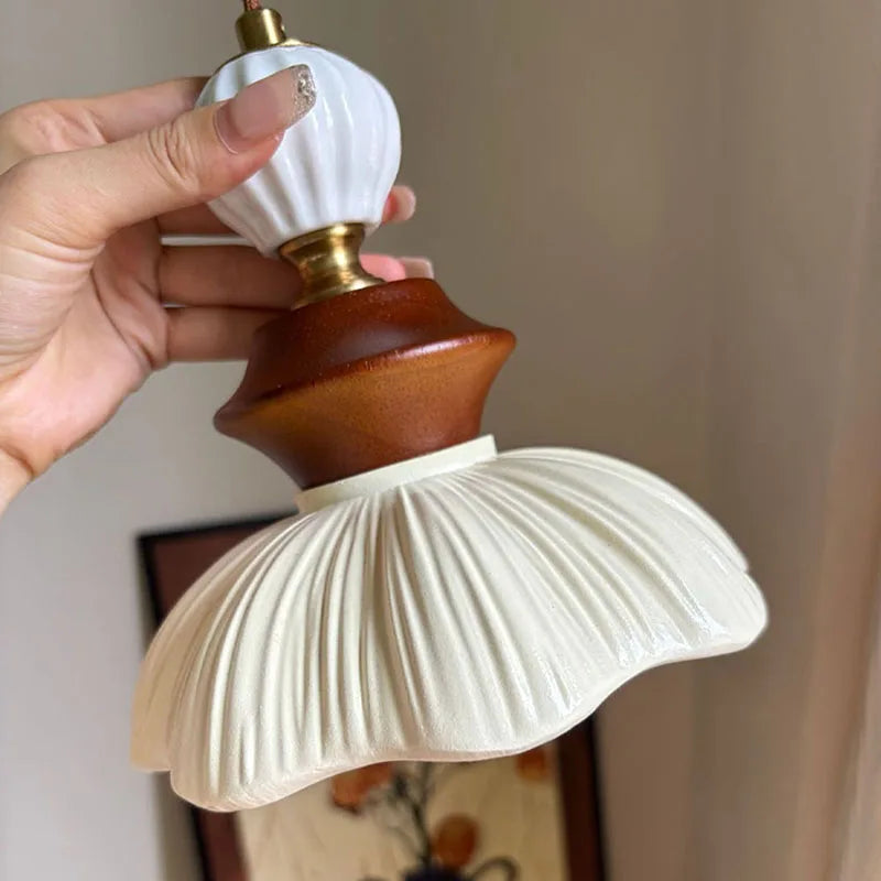 A hand holding the upper section of a resin and walnut pendant light, highlighting the ceramic top and brass hardware.