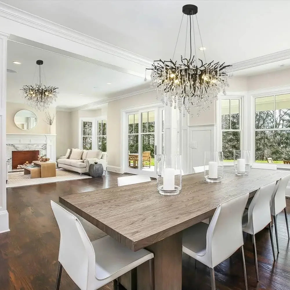 A black branch-style crystal chandelier hanging in a modern dining room with large windows and white chairs.