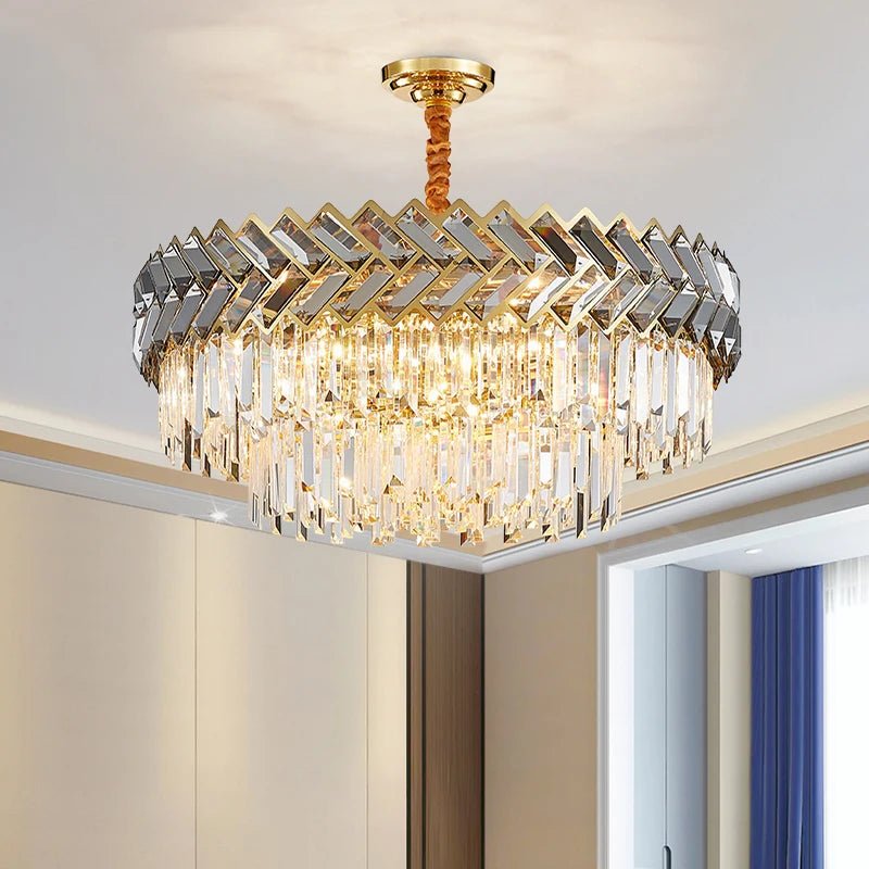 A gold-toned chandelier with multiple tiers of clear, rectangular crystals hanging in a cascading waterfall design, mounted on a white ceiling.