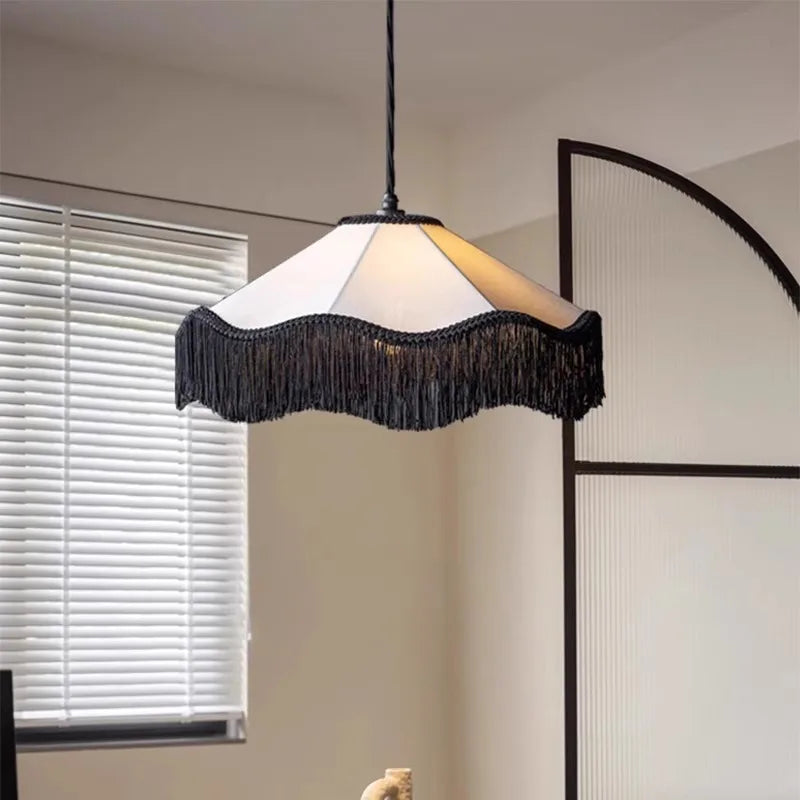 Black tassel fabric pendant light with a scalloped shade, suspended in a bright room near white blinds.