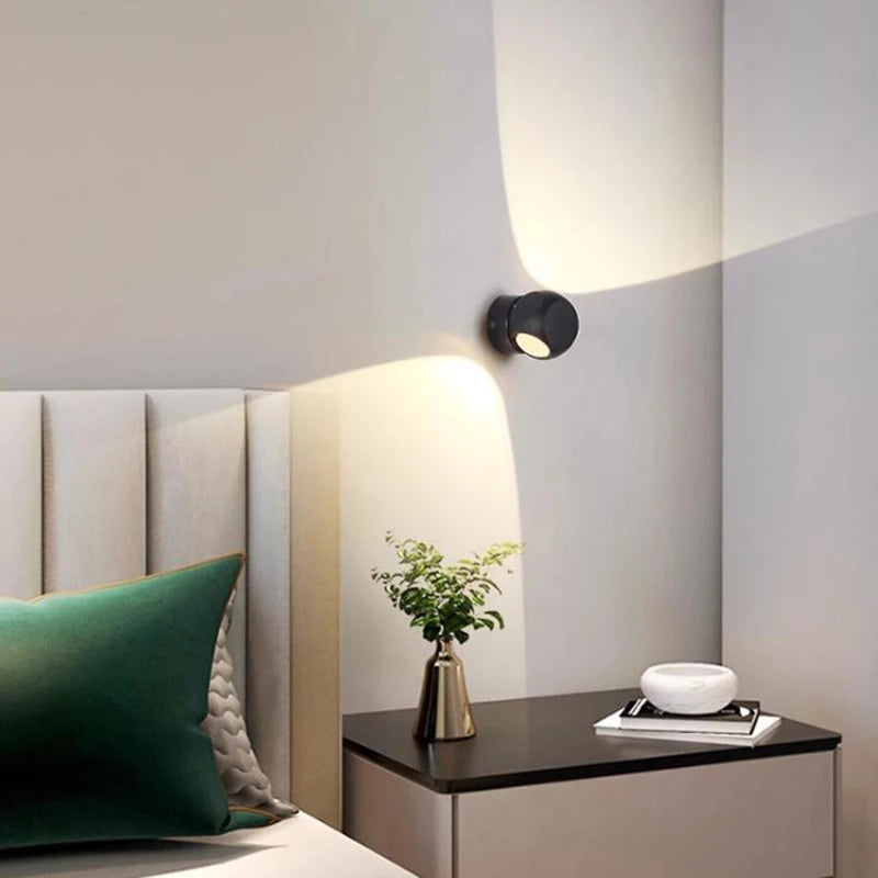 Modern wall light fixture on a neutral wall with a bed and nightstand in the foreground.