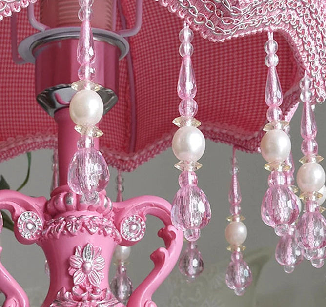 Pink chandelier with crystal and pearl decorations against a pink checkered background