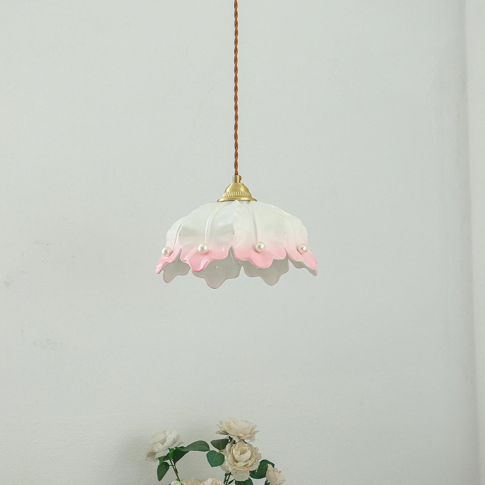 A side view of a pink and white ceramic petal pendant light with pearl accents, hanging against a white wall.