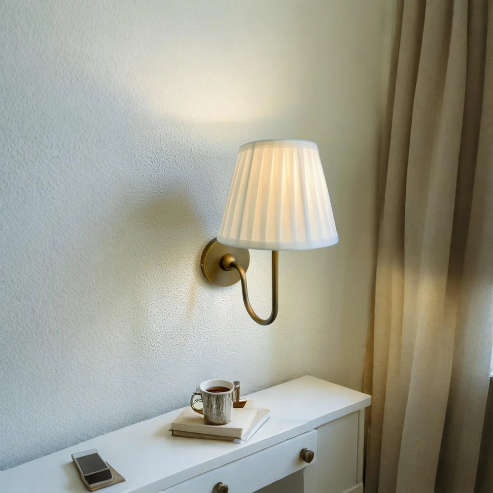Wall-mounted lamp on a white dresser with a cup and book next to it, against a neutral wall.