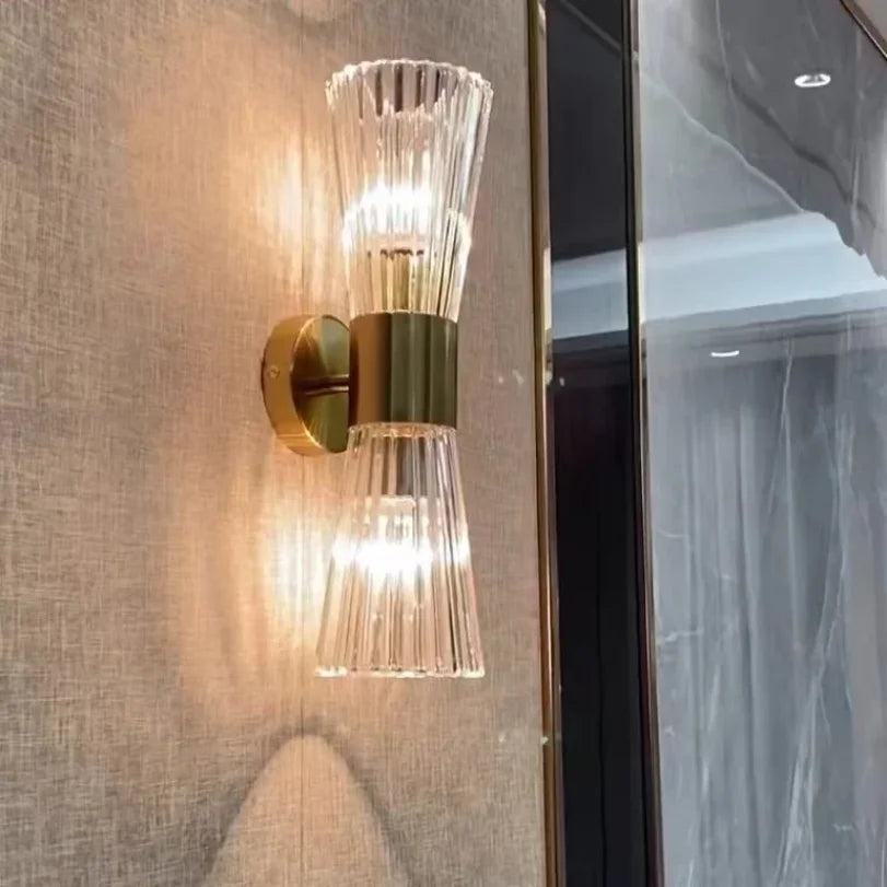 Wall-mounted light fixture with gold and clear glass design on a textured wall.