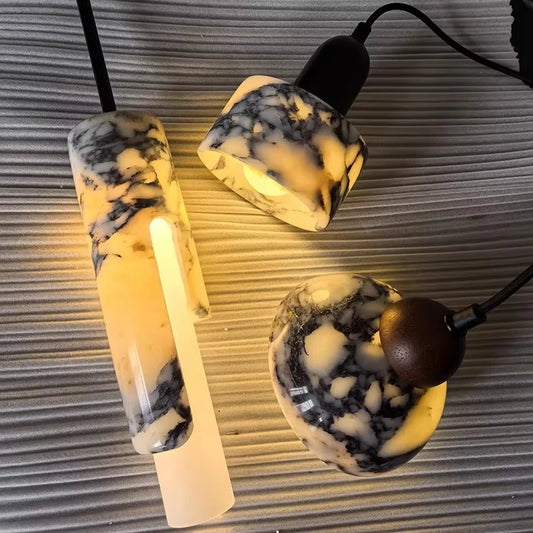 Close-up view of three marble and wood pendant lights arranged on a textured grey surface, highlighting their materials and illuminated glow.