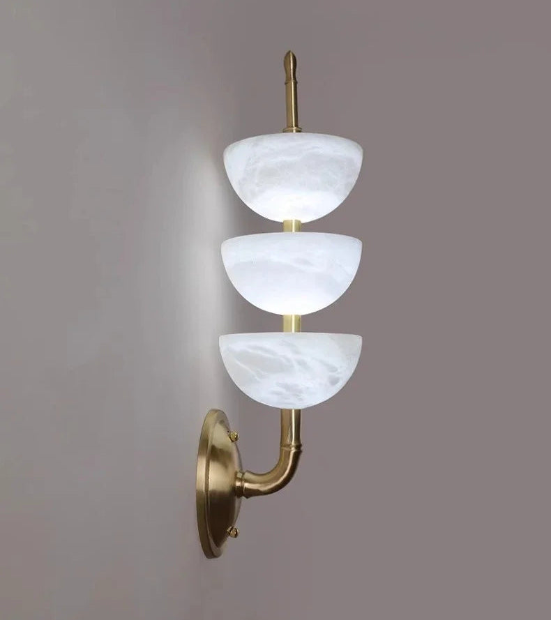 Wall-mounted light fixture with three white glass shades and gold metal arm on a gray background