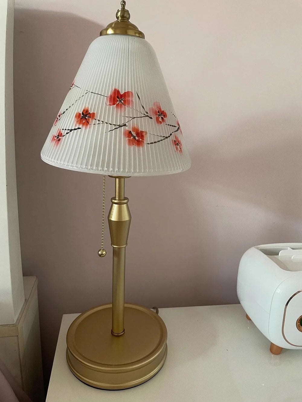 Decorative lamp with floral-patterned shade on a white surface against a pink wall