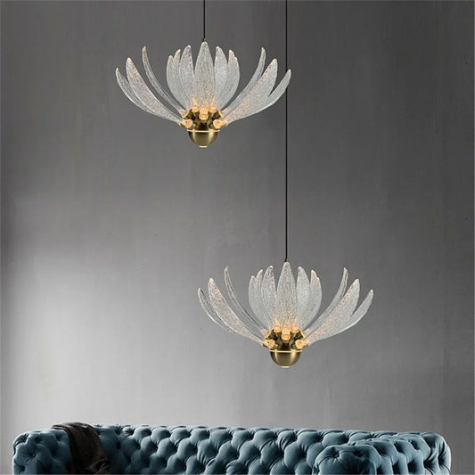 Two clear acrylic lotus flower pendant lights hanging over a plush blue sofa against a dark gray wall.