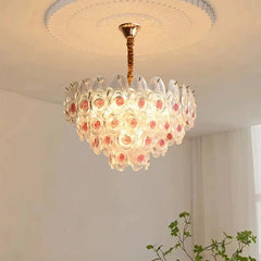 Brushed gold chandelier with clear glass and pink rose accents, in a close-up view.
