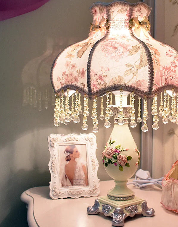 Decorative table lamp with pink floral shade on a table.