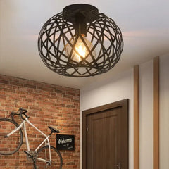 Black open cage semi-flush ceiling light with an exposed bulb, mounted in a hallway with brick wall.