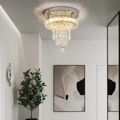 A chrome and crystal tiered ring flush mount ceiling light installed in a modern interior with abstract art and a plant.