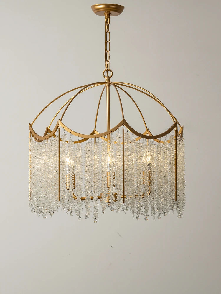 Close-up view of a gold-finished chandelier with cascading clear crystal droplets and internal lights against a plain background.