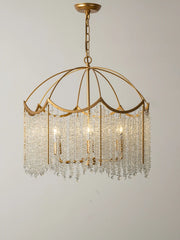 Close-up view of a gold-finished chandelier with cascading clear crystal droplets and internal lights against a plain background.