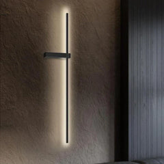 A close-up of a black minimalist LED strip wall sconce mounted on a dark textured wall, emitting soft light.
