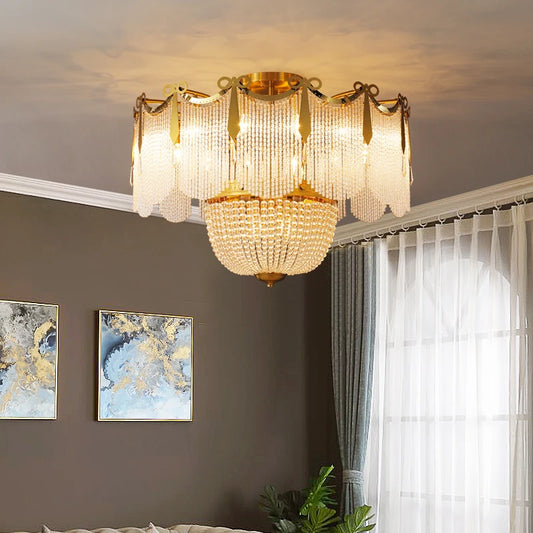A gold and crystal tiered chandelier hanging in a room with neutral curtains and artwork.
