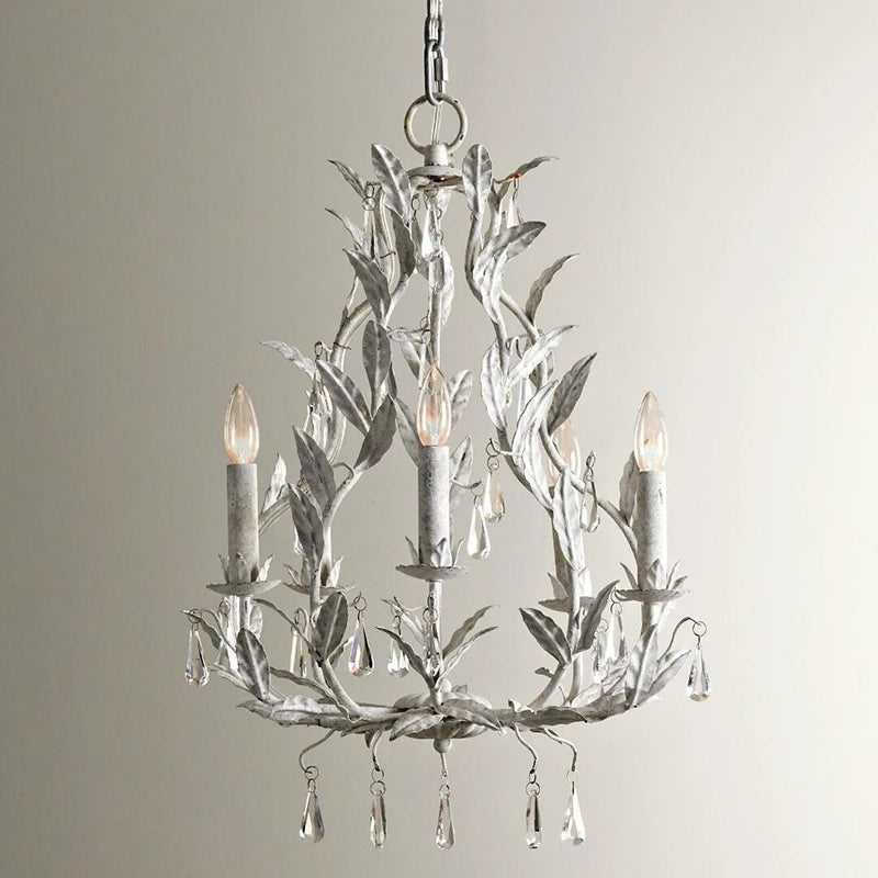 Light grey wrought iron leaf chandelier with clear teardrop crystals hanging from candle-style lights, against a white background.