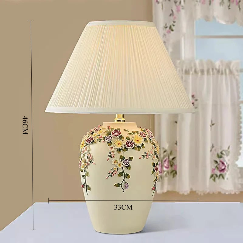 Decorative table lamp with floral design and pleated shade on a neutral background