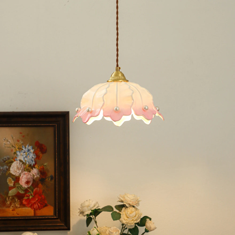A pink and white ceramic petal pendant light with pearls, shown in a room setting next to a painting and flowers.
