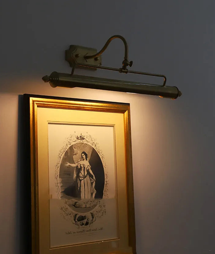 Wall-mounted light fixture casting a warm glow on a framed picture of a woman in a gold frame.