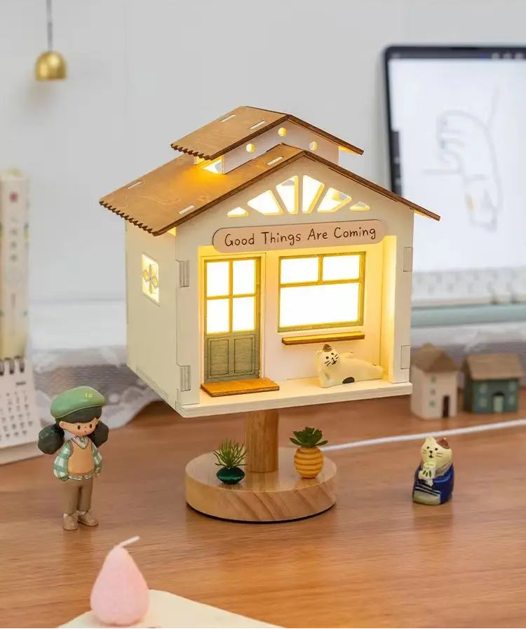 A whimsical white tree house table lamp on a wooden base, featuring a playful cat figurine and a girl figurine beside it.
