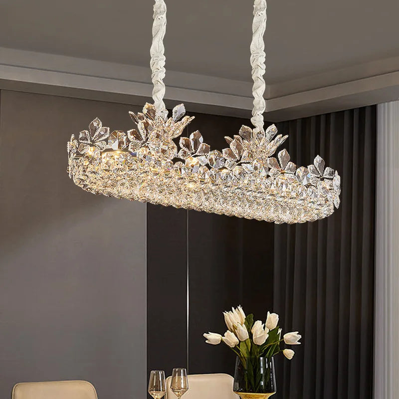 Polished chrome linear chandelier with crystal floral accents, suspended over a dining table.
