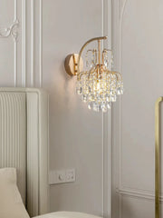 Gold crystal wall sconce mounted above a tufted headboard in a bedroom setting.