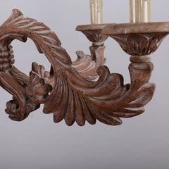 Detailed view of the carved wooden arms and floral motifs on a distressed wood candelabra chandelier.