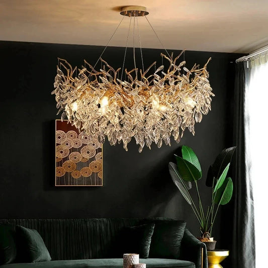 A close-up of a gold-toned chandelier with crystal leaves and branches, illuminated in a dimly lit room with dark walls.