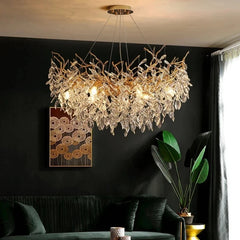A close-up of a gold-toned chandelier with crystal leaves and branches, illuminated in a dimly lit room with dark walls.