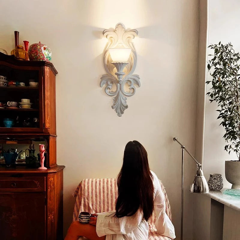 Woman sitting on a chair in a room with a decorative wall light fixture.