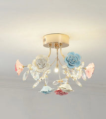 A flush mount ceiling light with a gold base, featuring white, blue, and pink ceramic roses and crystals.