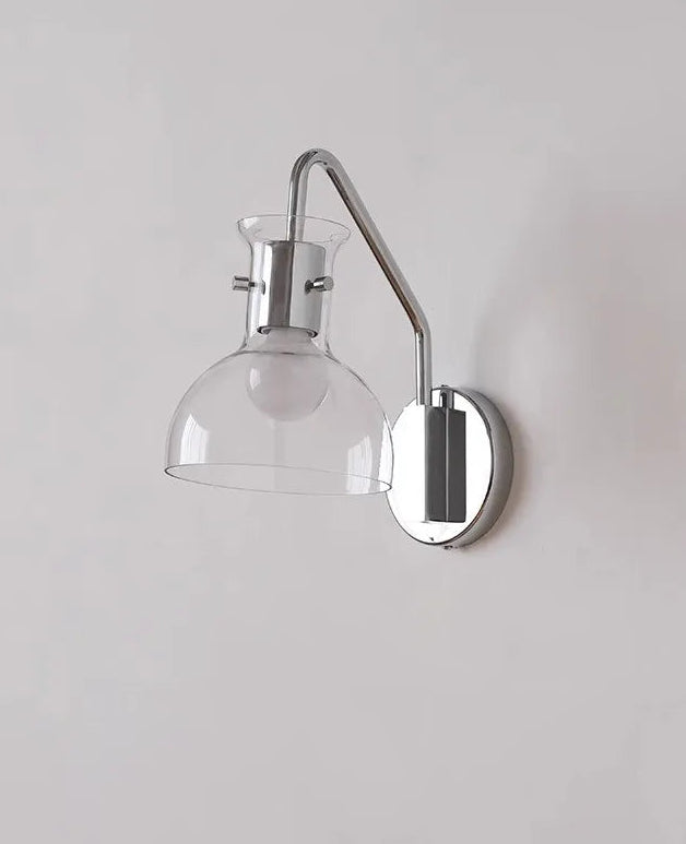Wall-mounted lamp with clear glass shade and chrome finish on a light gray wall.