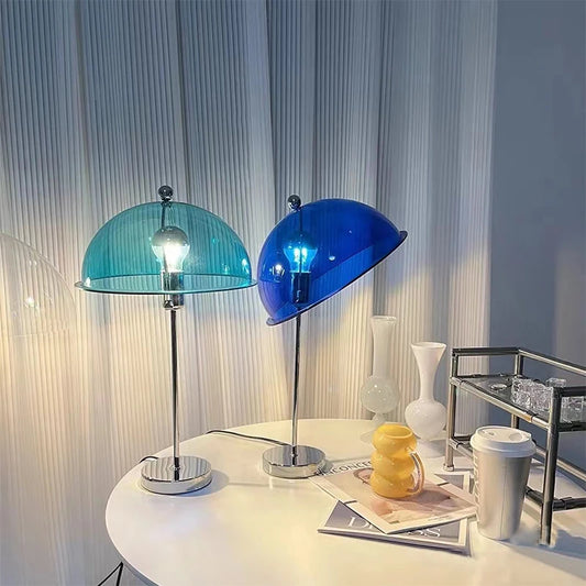 Two mushroom-shaped table lamps with blue and teal glass shades on a white table with white curtains in the background.